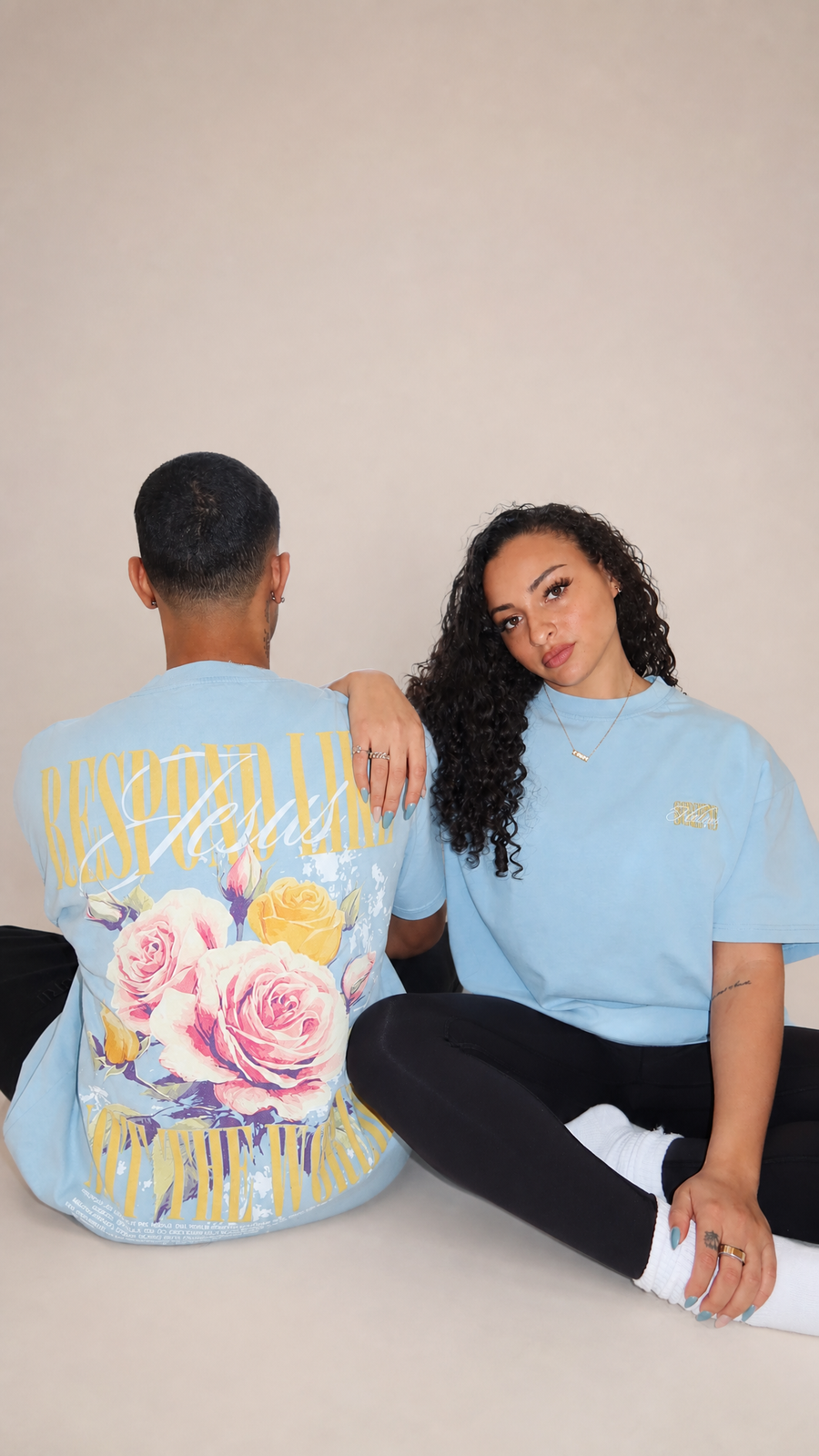 Woman wearing light blue "Respond Like Jesus" Christian tee with floral back graphic - sitting pose