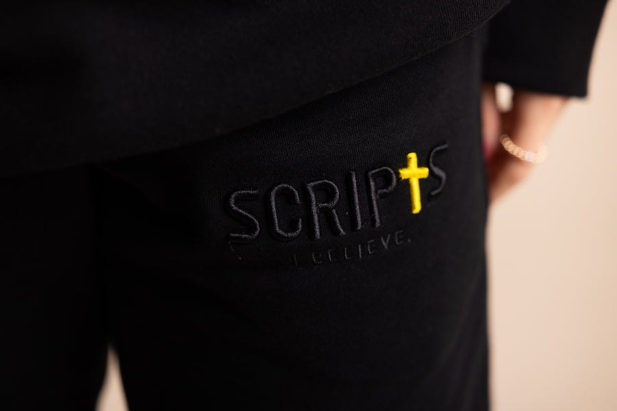 Close-up of "SCRIPTS" embroidered logo with cross on black fleece sweatpants