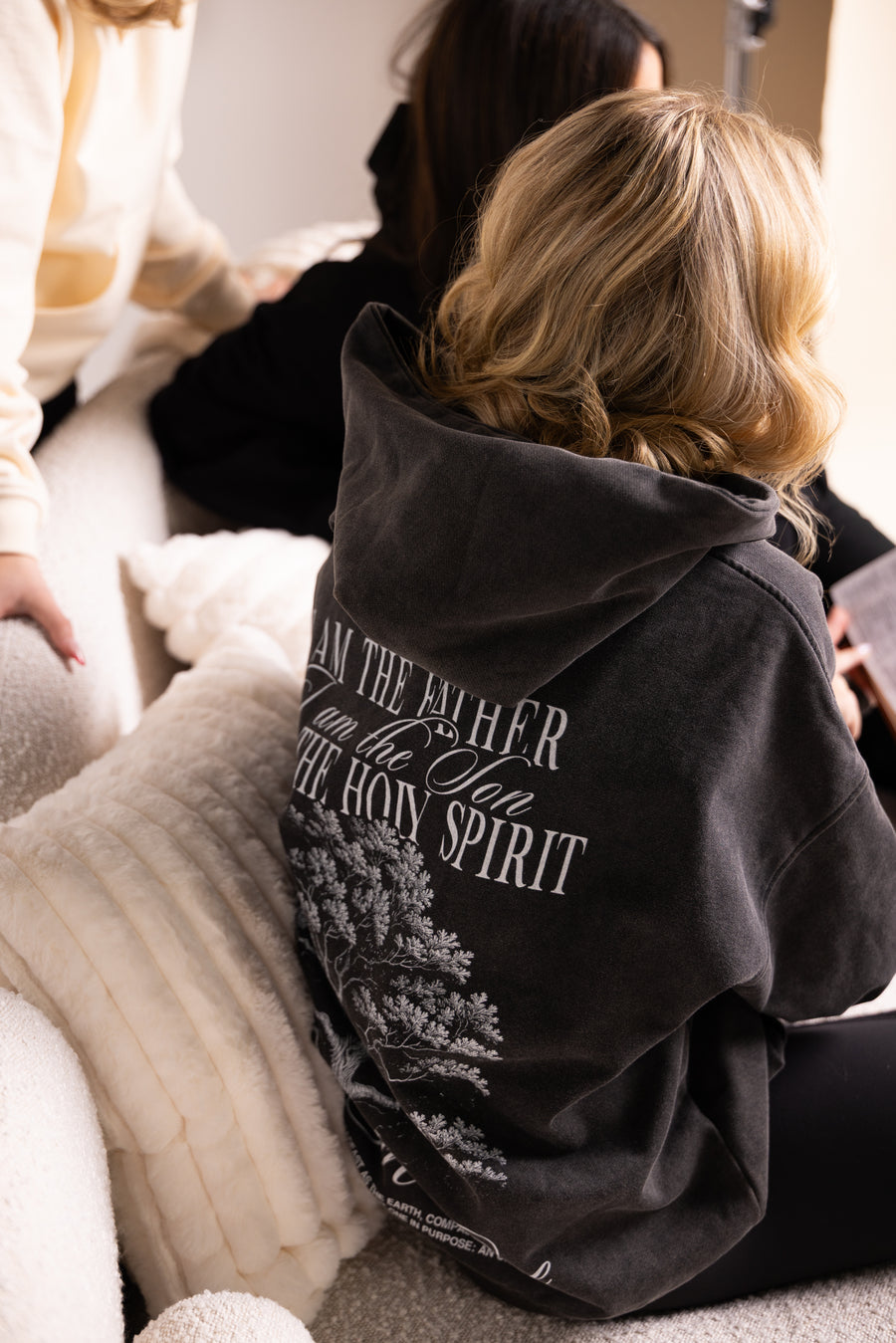 Two girls wearing black Holy Trinity Christian hoodies with tree graphic - back view