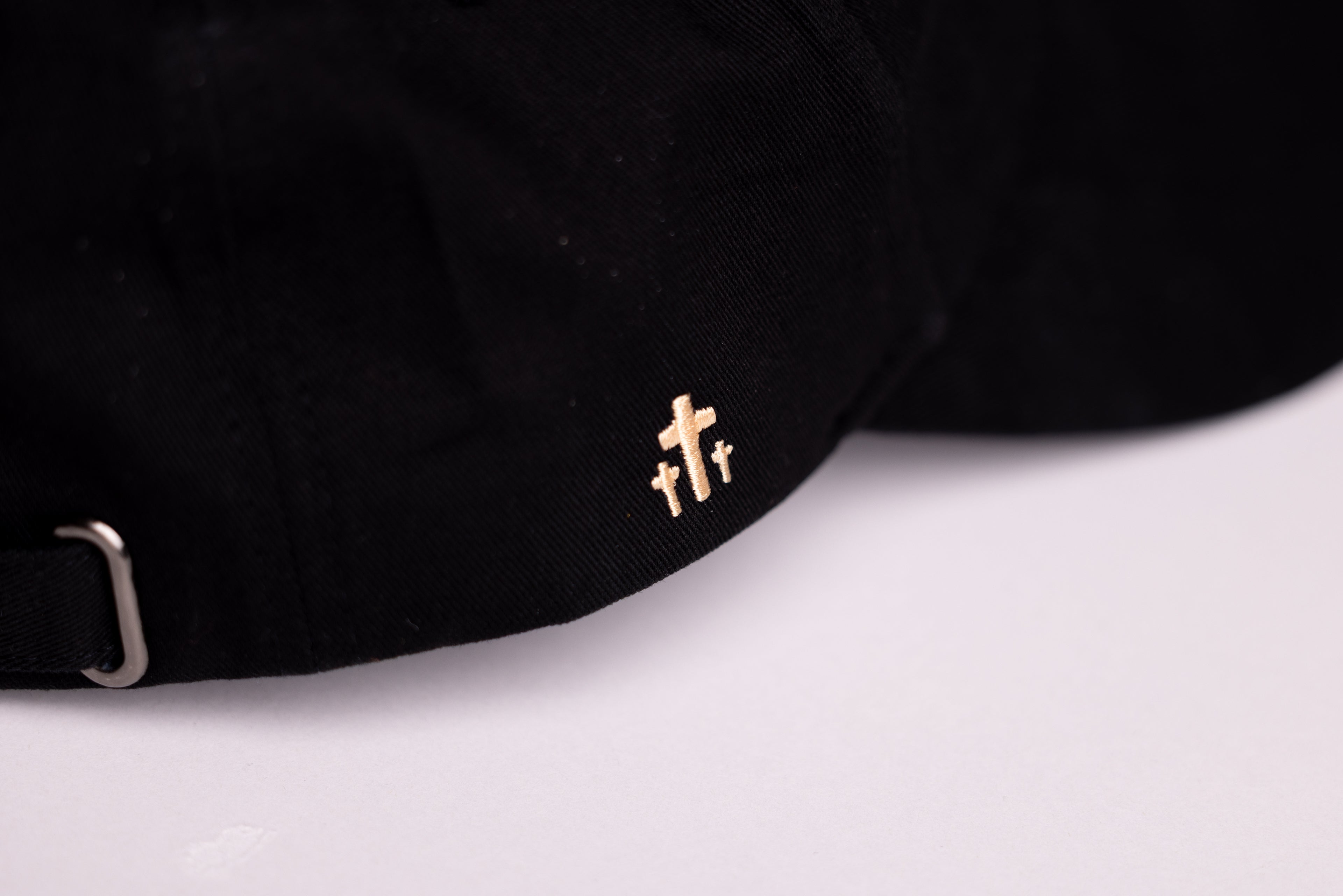 Close-up of gold cross embroidery on black Christian baseball cap