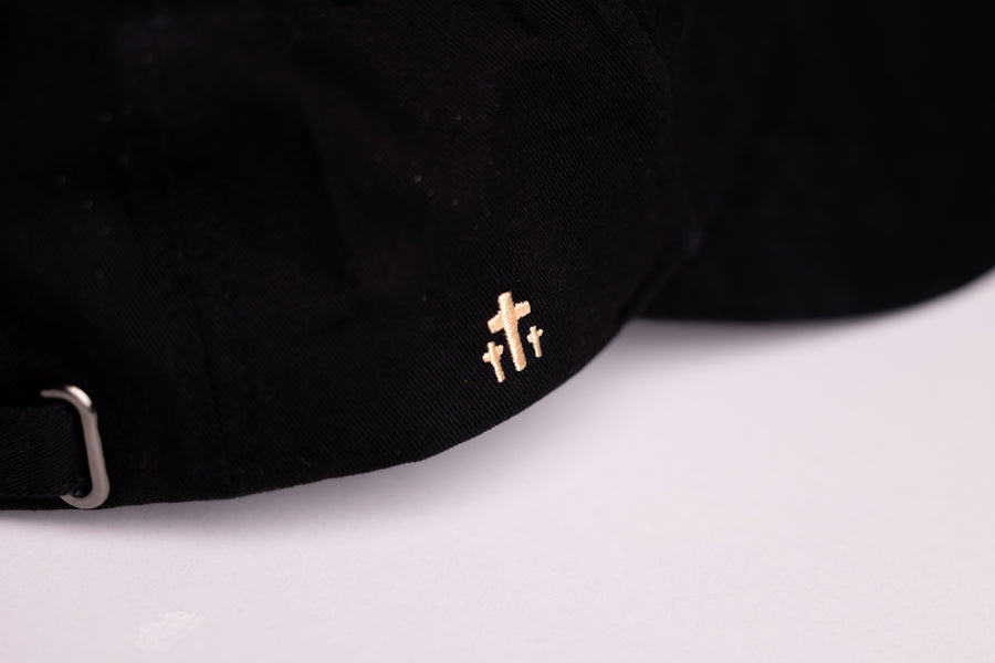 Close-up of gold cross embroidery on black Christian baseball cap