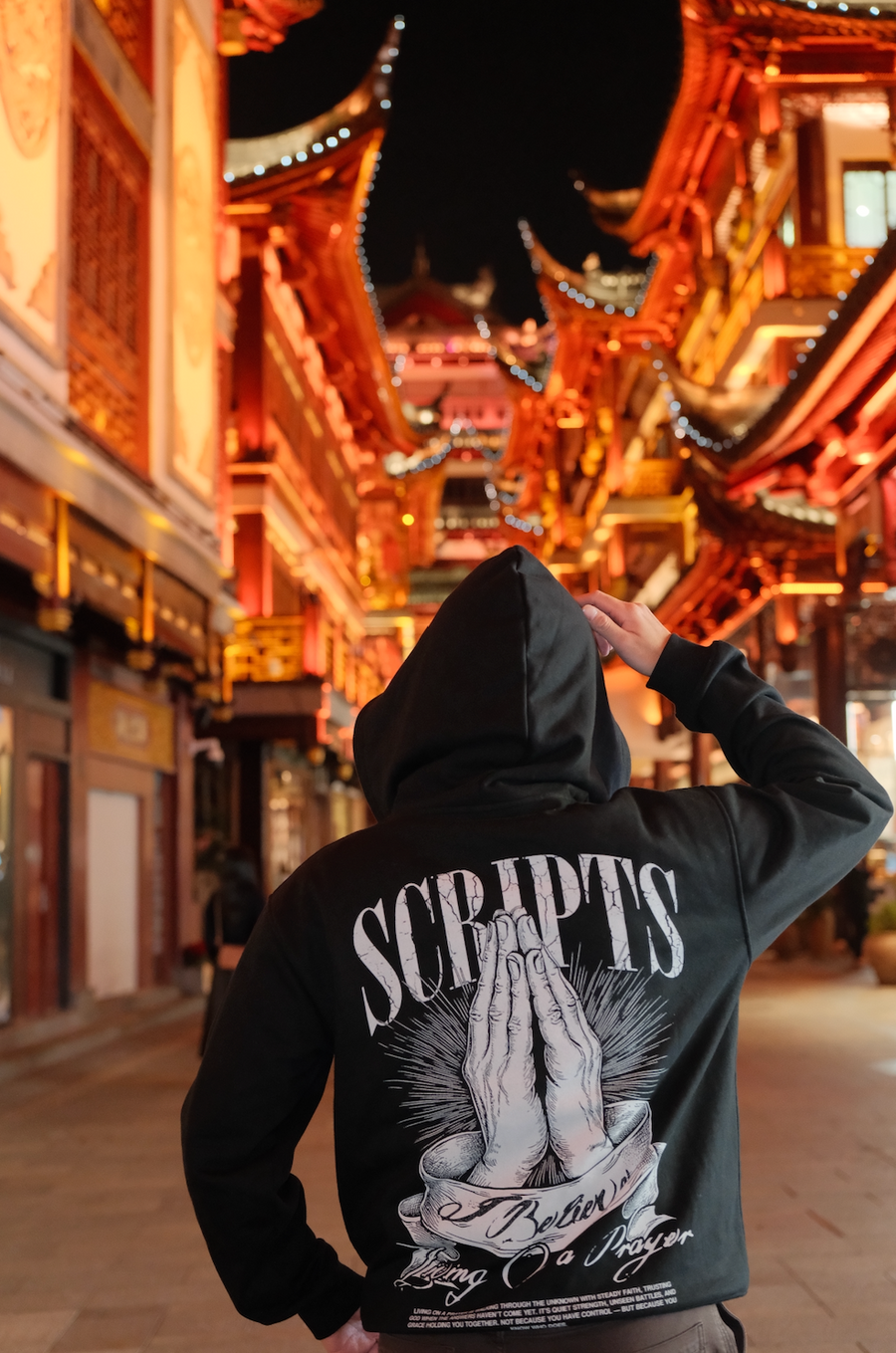 Man wearing black "Living On A Prayer" Christian hoodie - walking outdoors at night