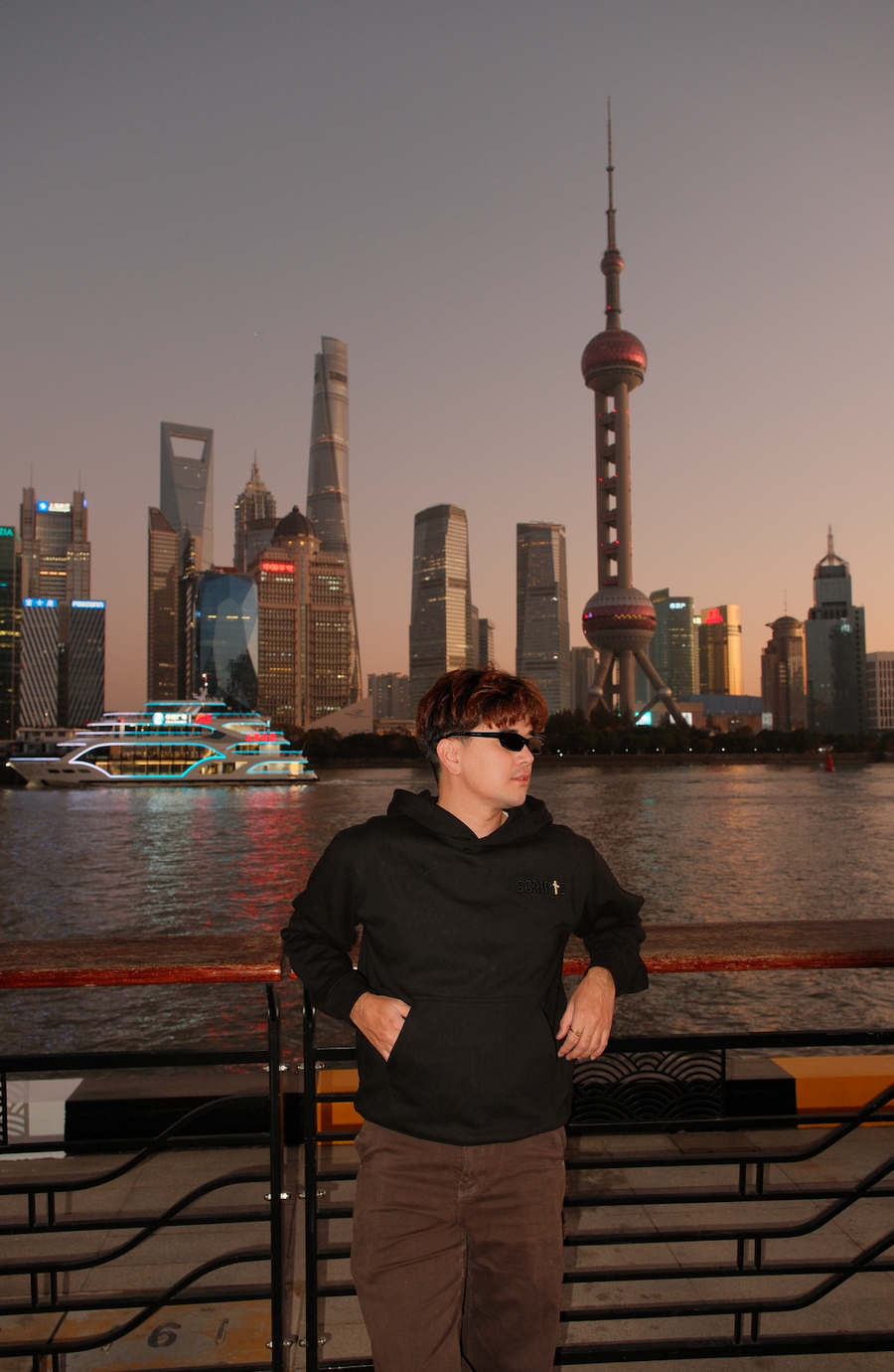 Man wearing black "Living On A Prayer" Christian hoodie - city skyline at sunset